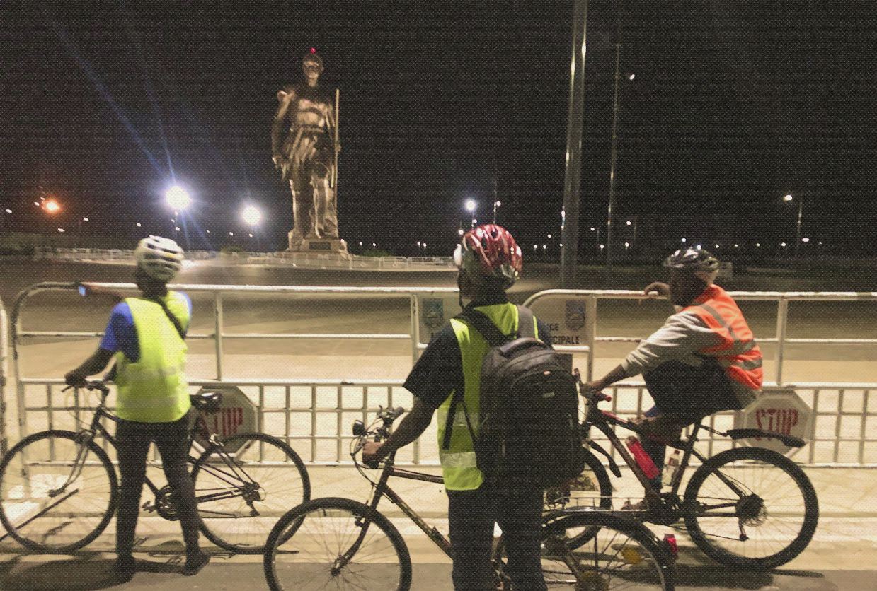 Cyclistes devant la statue de l'Amazone lors d'une visite nocturne de Cotonou